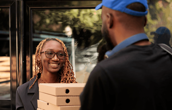 smiling woman receiving order from courier near office building